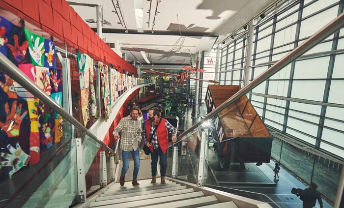 two men are walking up an open stair case inside a light, modern gallery. Behind them you can see a large coal truck that would have been pulled by tr